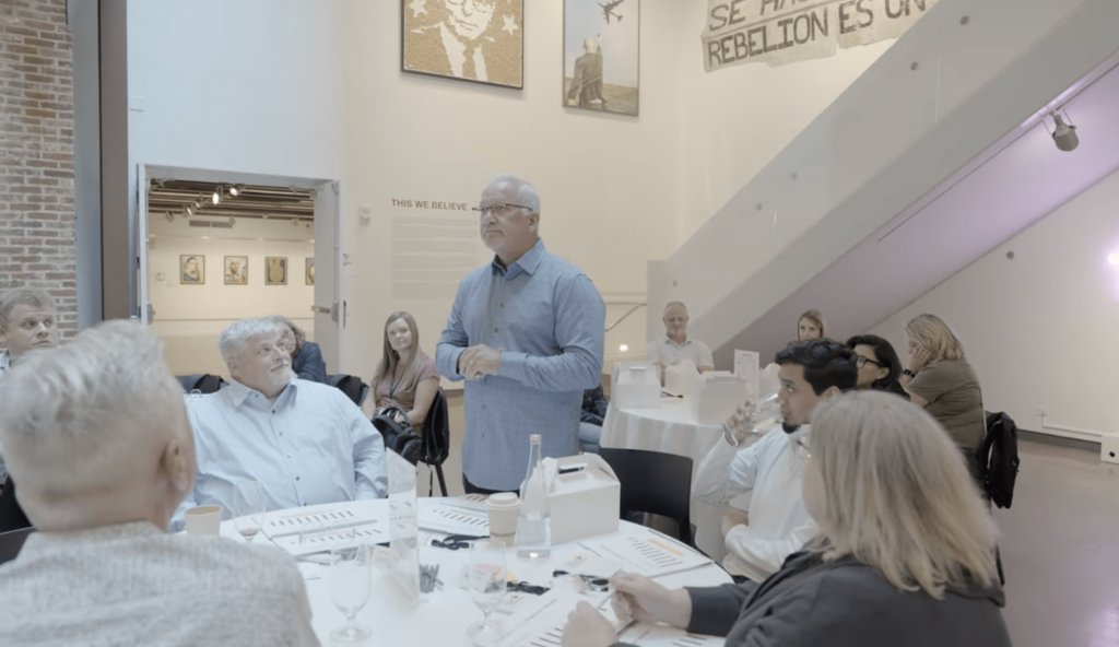 A man standing up from his seat to speak to an event room